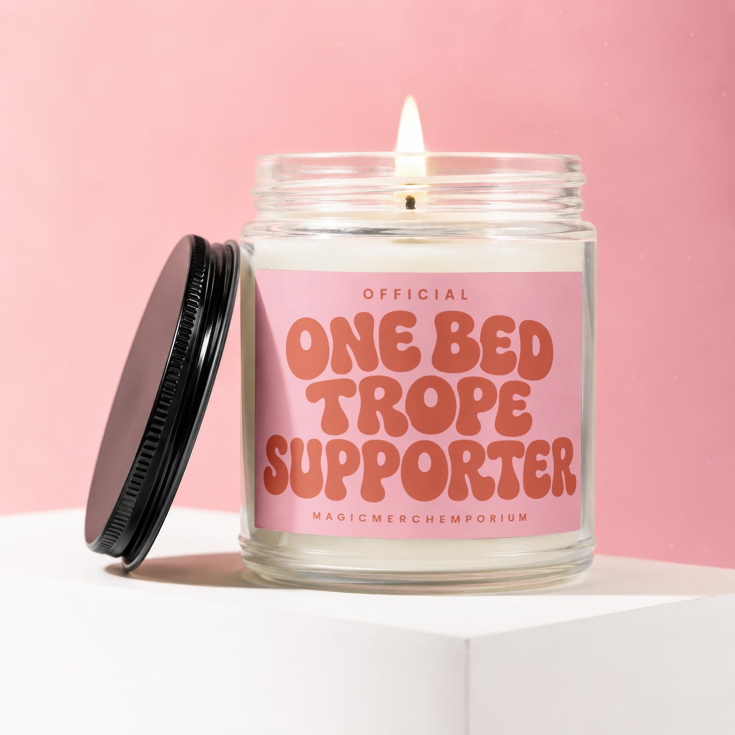 Glass candle with flame and pink label reading "OFFICIAL ONE BED TROPE SUPPORTER".