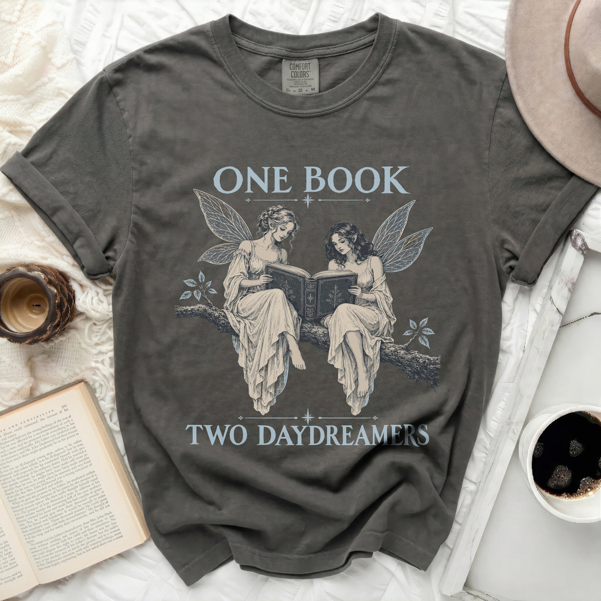 Dark grey t-shirt with graphic of two fairies reading a book, text "ONE BOOK TWO DAYDREAMERS".