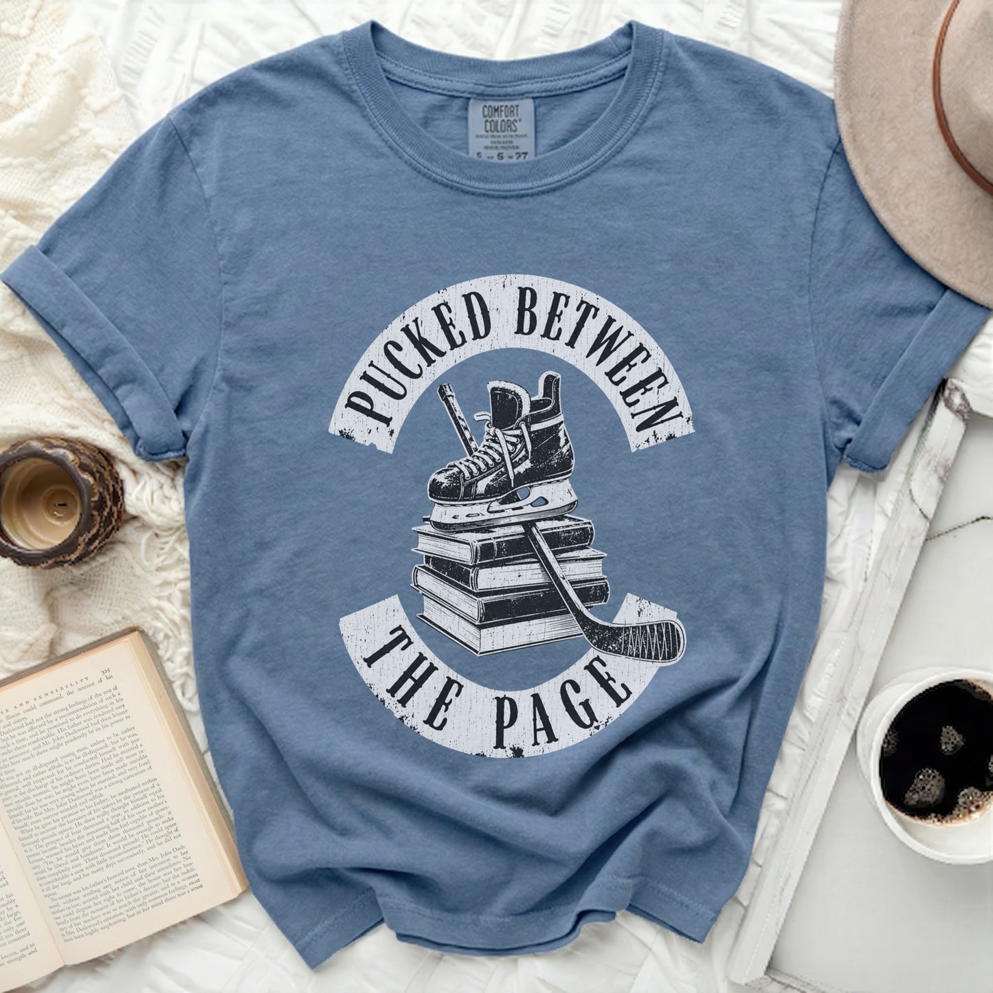 Blue t-shirt with "Pucked Between the Page" text and hockey skates on books.
