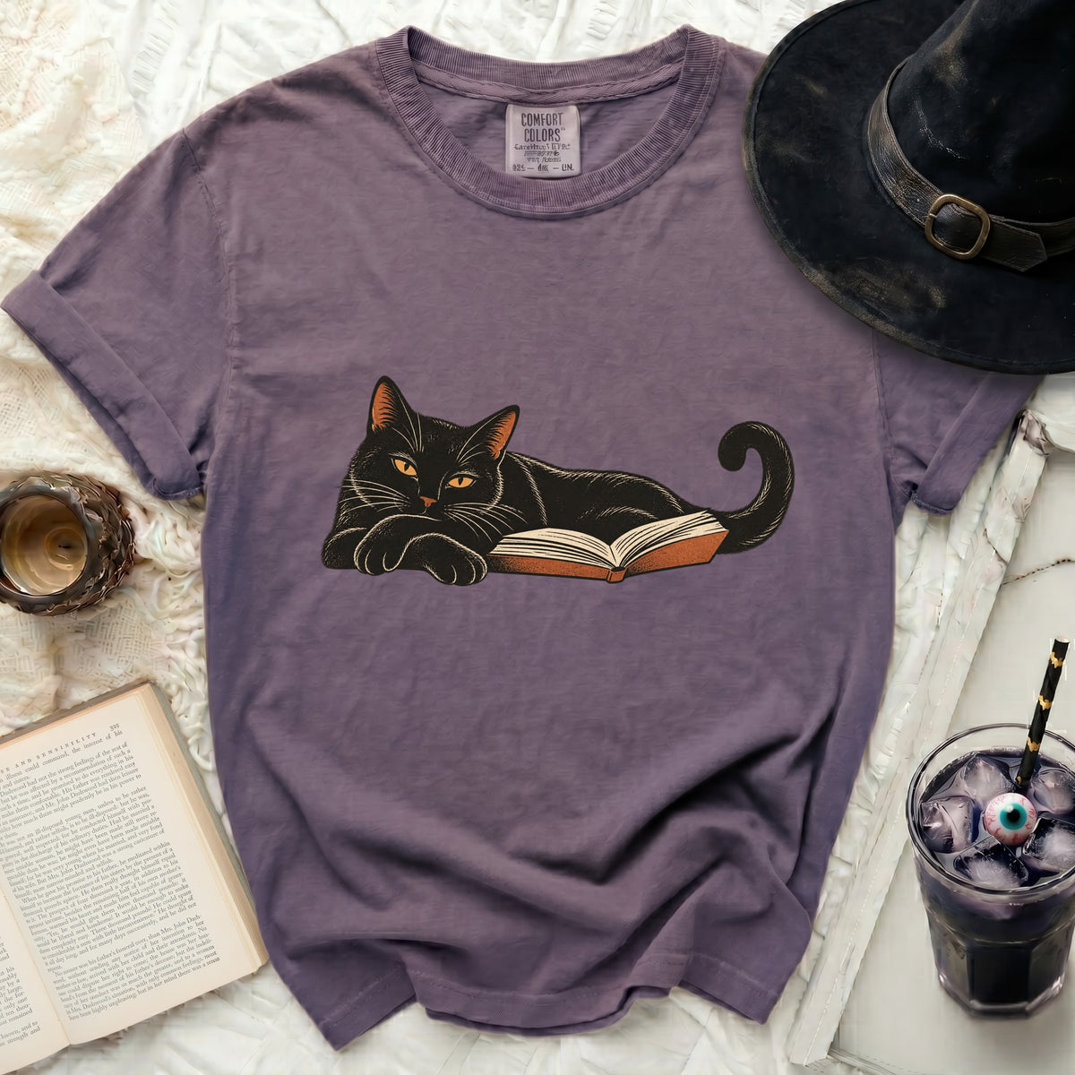Purple t-shirt with black cat lying on an open book design.