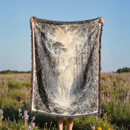 A person holds up a large blanket with a deer image on it, standing in a field with purple flowers.