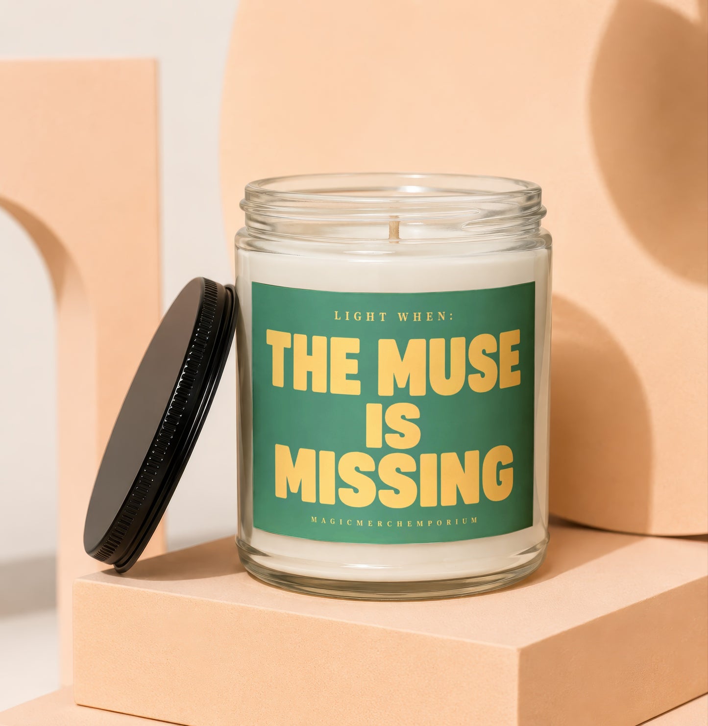 Glass candle with green label reading "Light When: The Muse Is Missing"