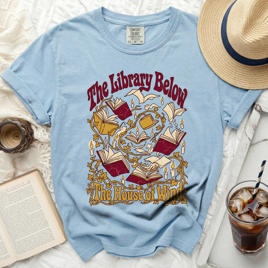 Light blue t-shirt with "The Library Below The House of Win" text and book graphic.