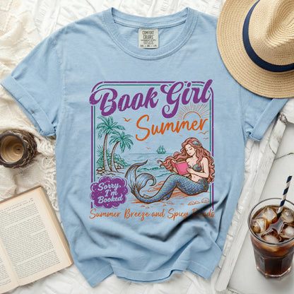 Light blue t-shirt with a mermaid reading a book on a tropical beach design.