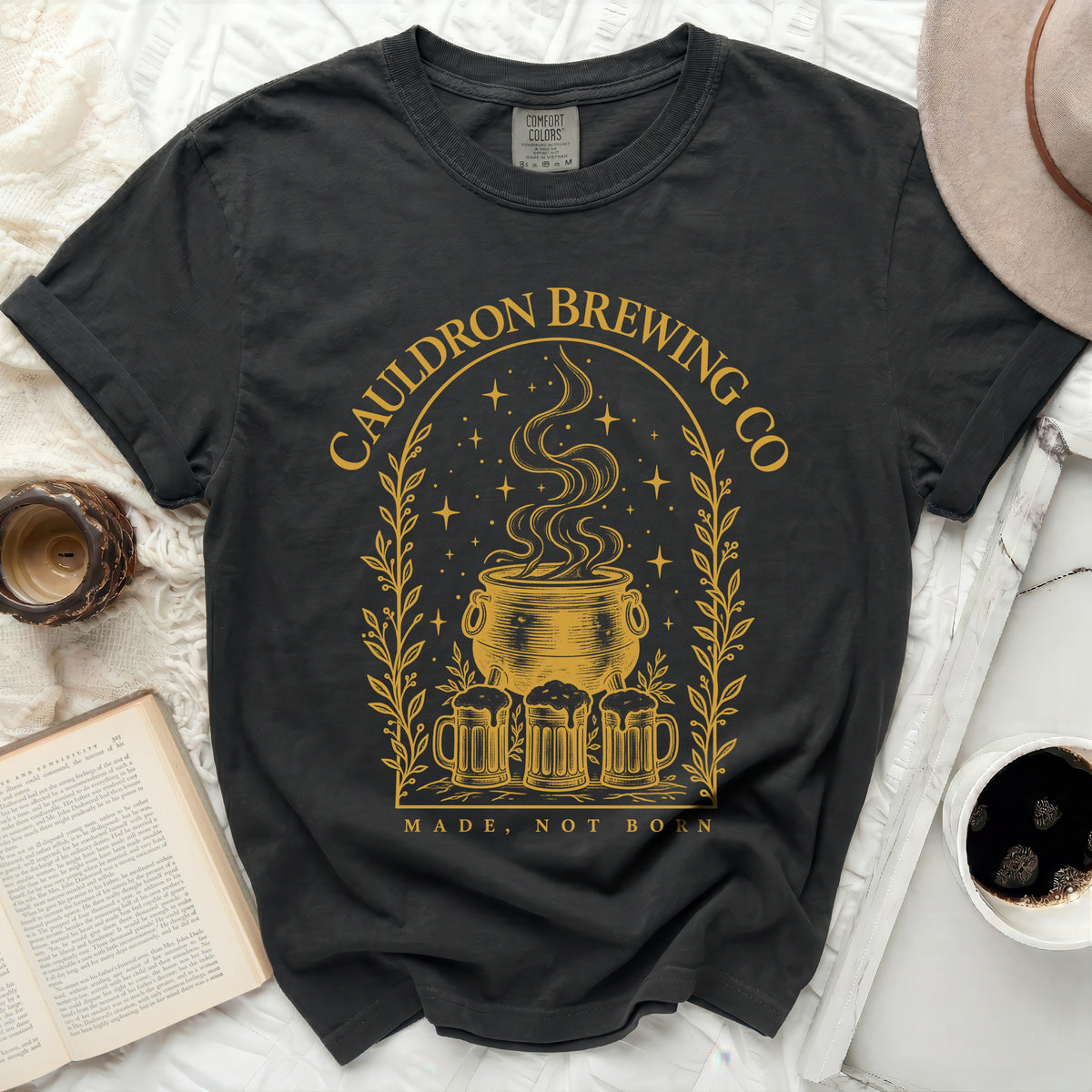 A black crewneck t-shirt featuring a gold graphic of a steaming cauldron, beer mugs, and text.
