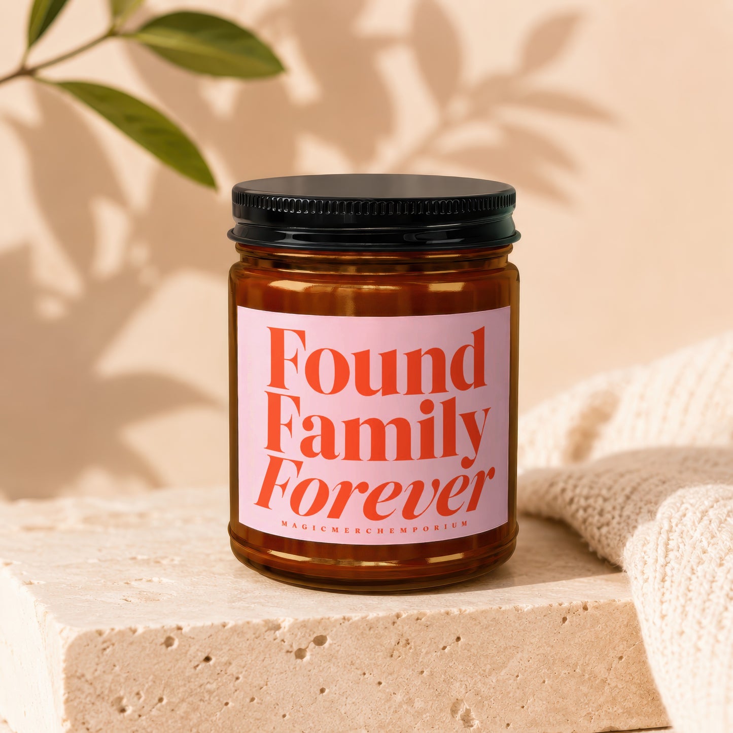 Amber jar candle with pink label reading "Found Family Forever" and "Magic Merch Emporium".