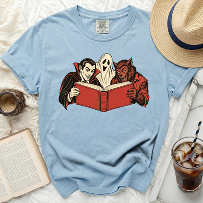 Vampire, ghost, and werewolf reading a book on a light blue t-shirt.