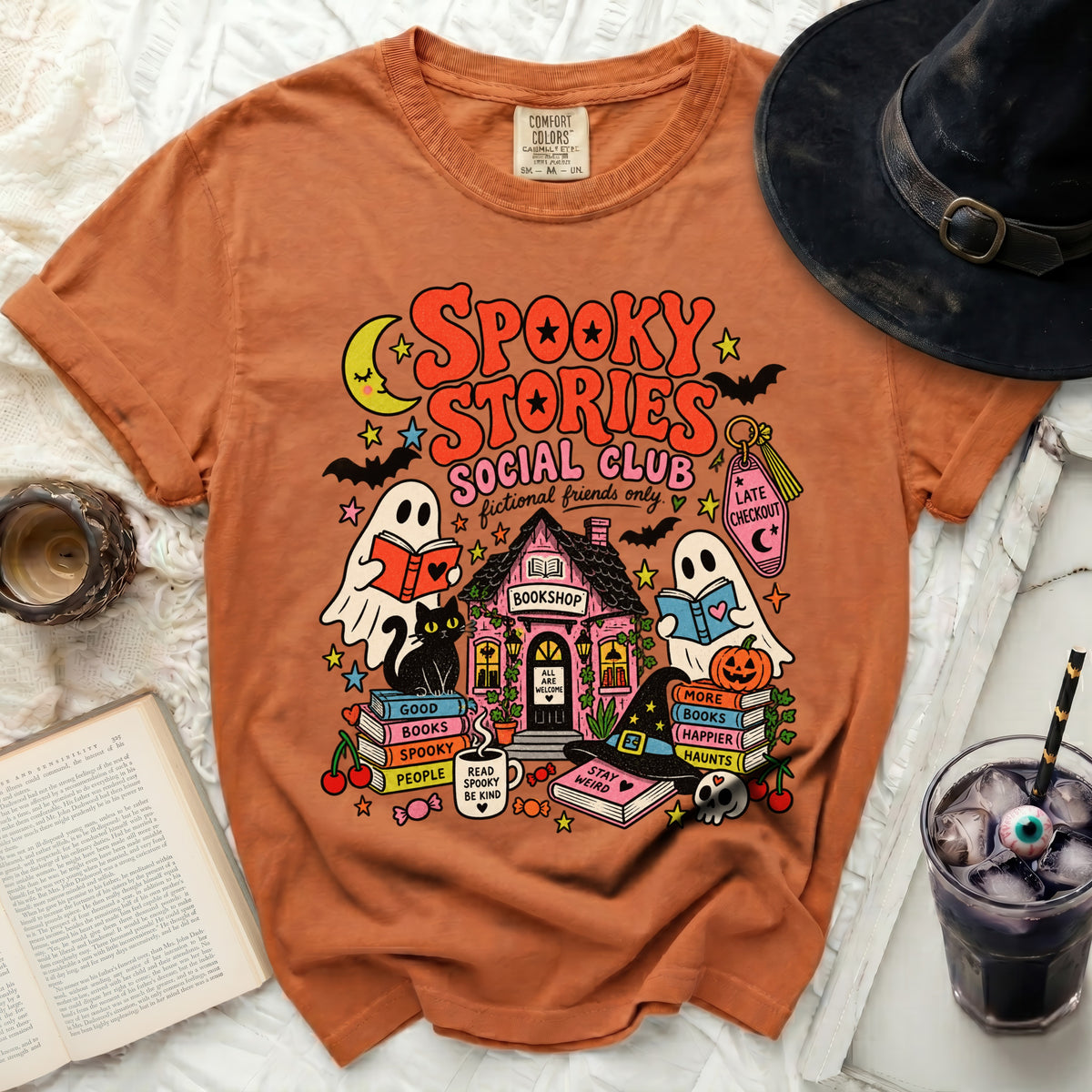 Orange t-shirt with a spooky Halloween book club graphic featuring ghosts, a cat, and a bookshop.