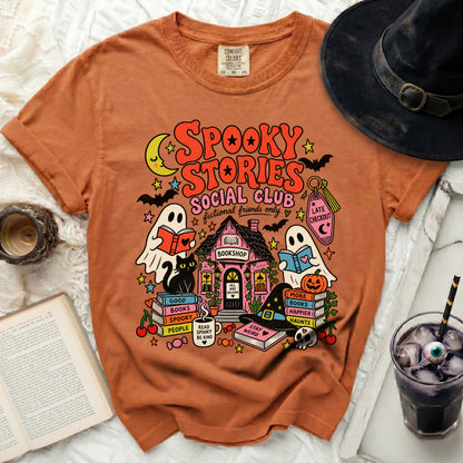 Orange t-shirt with a spooky Halloween book club graphic featuring ghosts, a cat, and a bookshop.