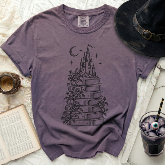 A dark purple t-shirt featuring a black graphic of a castle atop a stack of books with climbing roses.