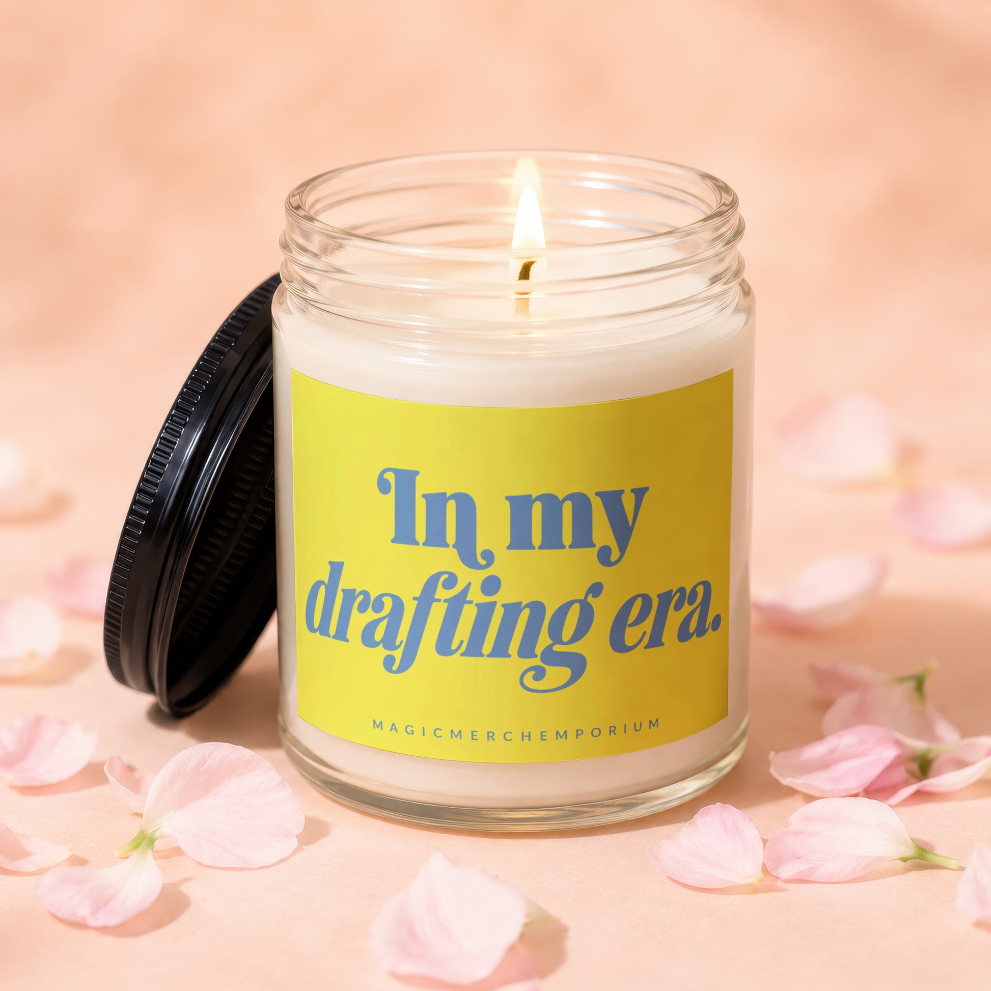 Glass candle with lit wick and yellow label saying "In my drafting era."