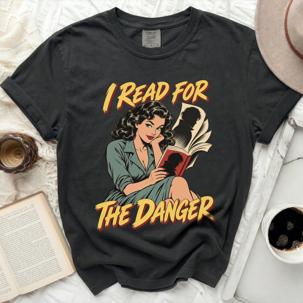 T-shirt featuring a vintage comic style graphic of a woman reading a book with text "I READ FOR THE DANGER".