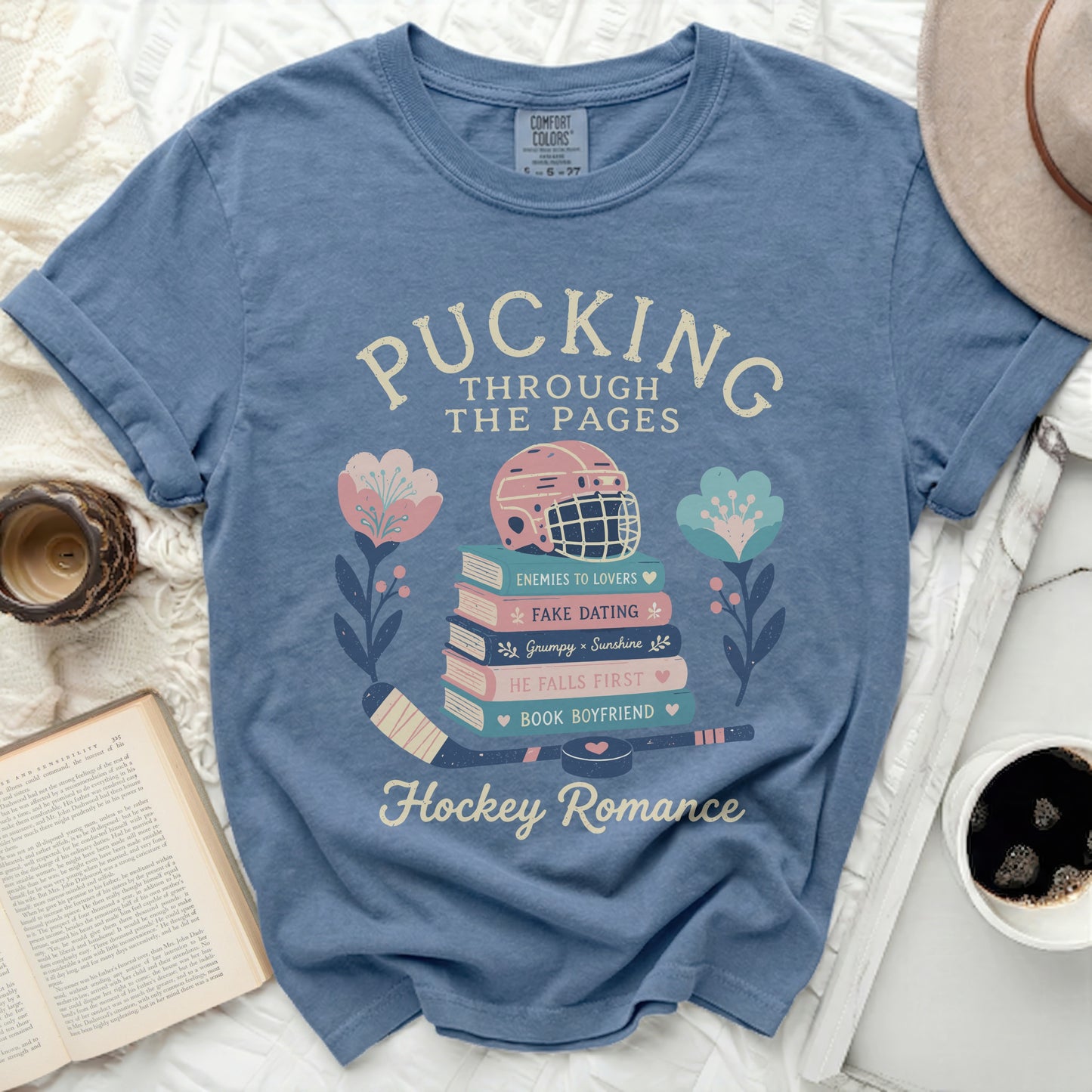 Blue t-shirt with "Pucking Through The Pages" and book/hockey themed graphics.