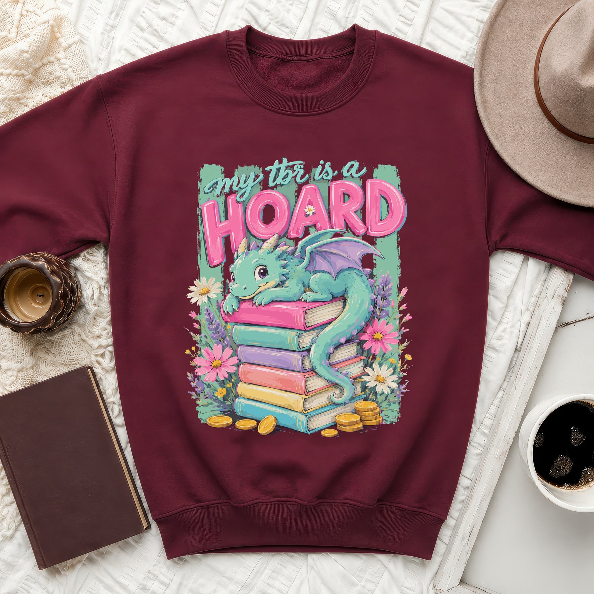 Maroon sweatshirt with a graphic of a dragon on stacked books that reads "My TBR is a HOARD."