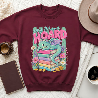 Maroon sweatshirt with a graphic of a dragon on stacked books that reads "My TBR is a HOARD."