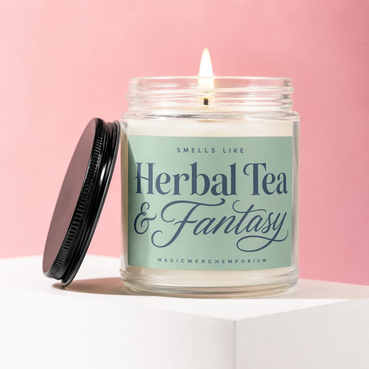 Glass jar candle with lit wick, labeled "Herbal Tea & Fantasy".