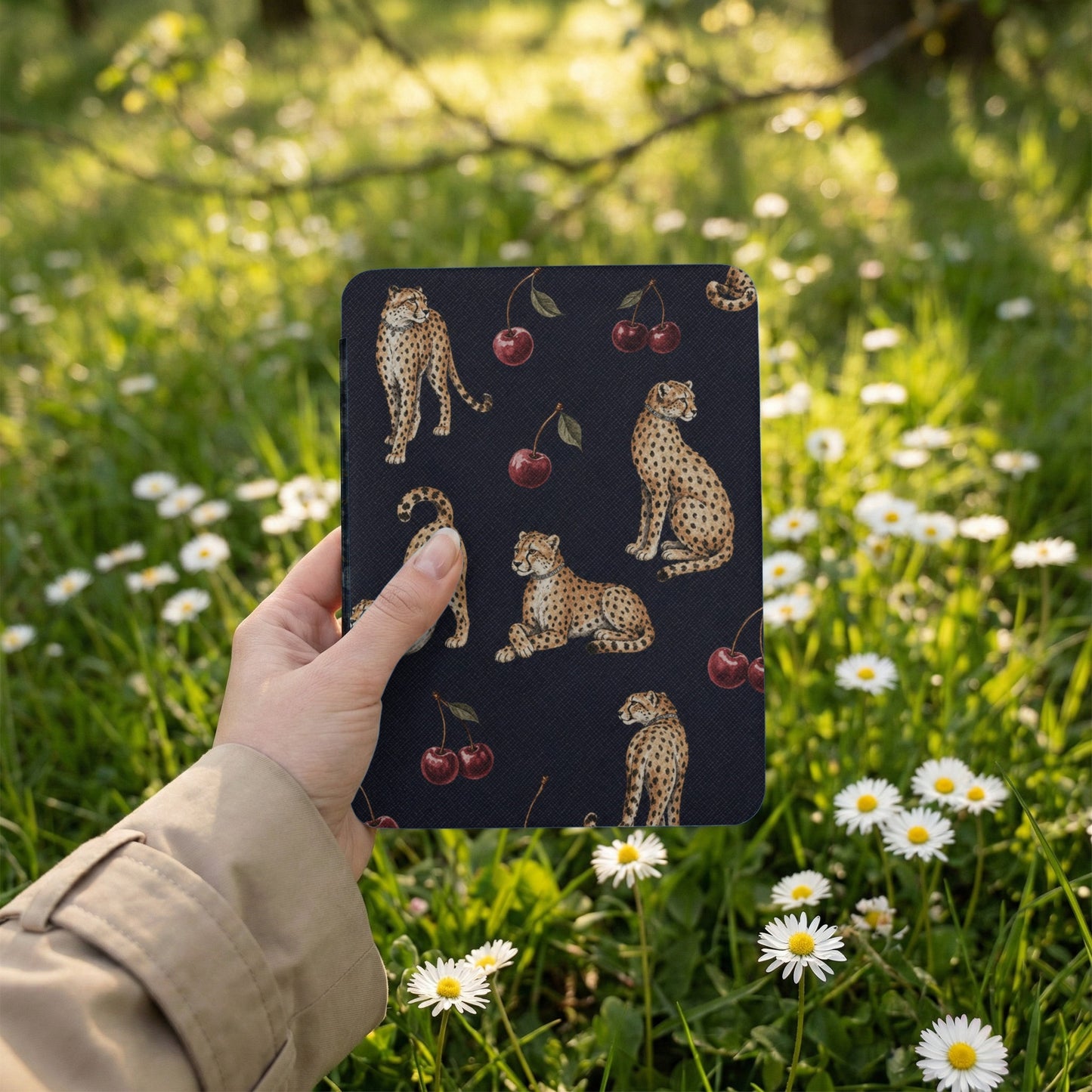 Dark blue cover with cheetah and cherry pattern, held outdoors among daisies.