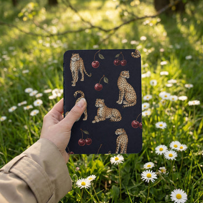 Dark blue cover with cheetah and cherry pattern, held outdoors among daisies.
