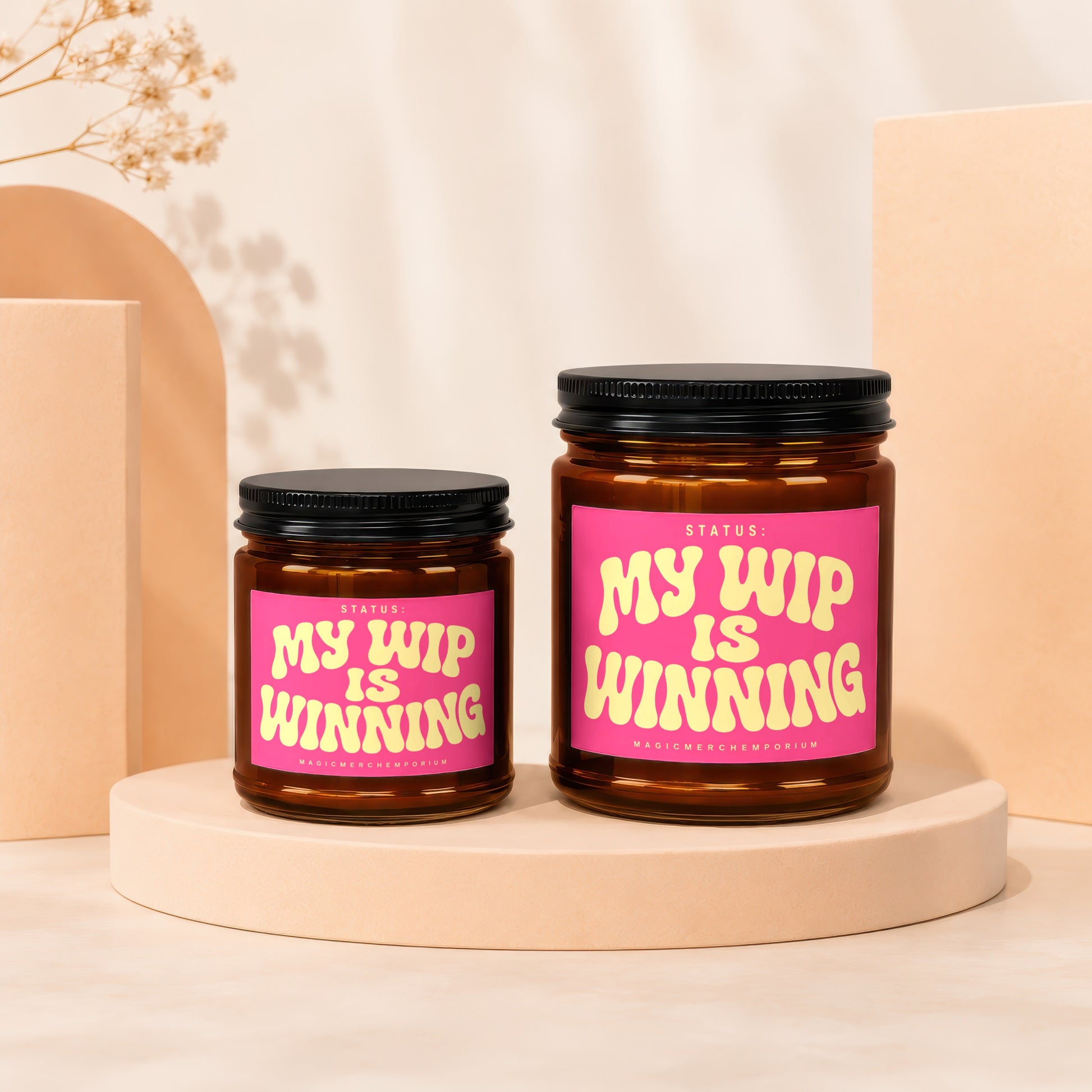 Two amber glass candles with pink labels reading "My WIP Is Winning" on display.