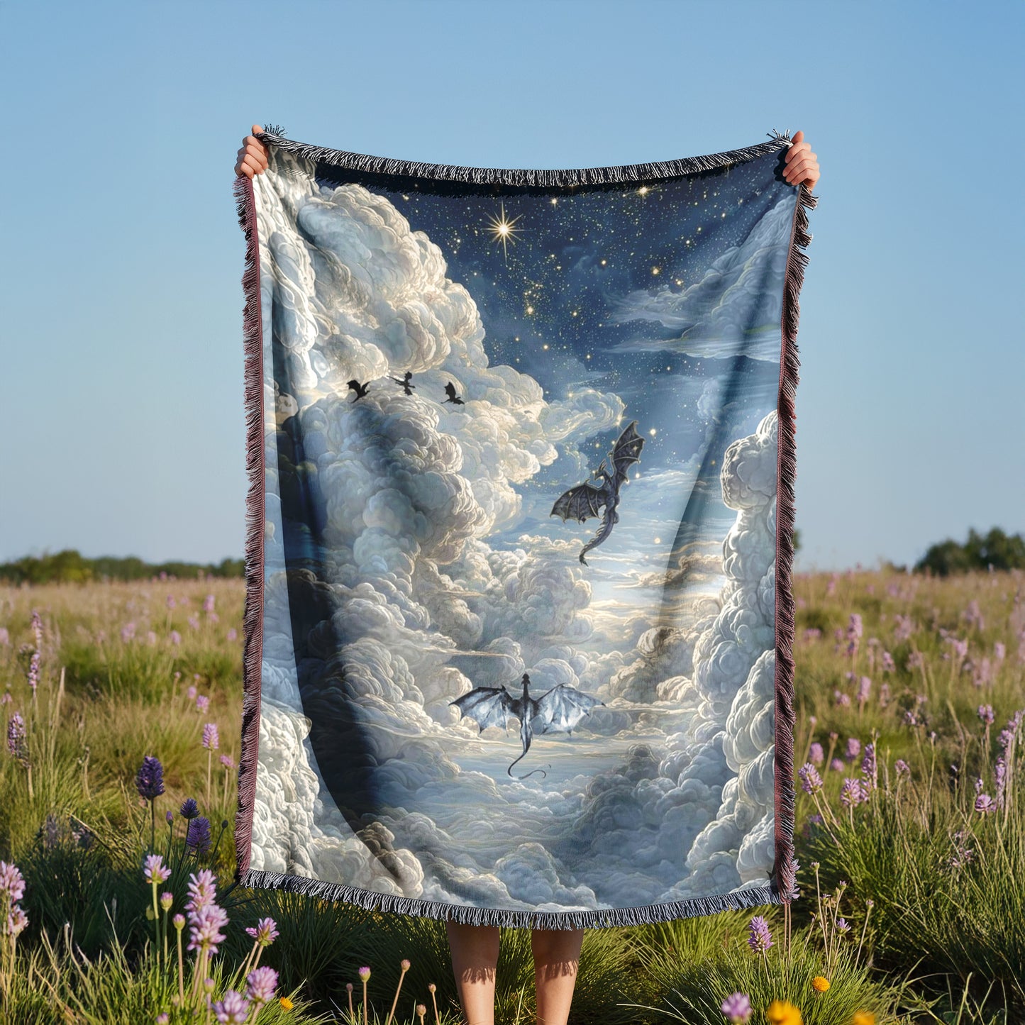 A person is holding up a large blanket with a dragon and clouds printed on it, standing in a field with purple flowers.