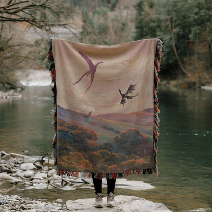 A person stands on a rock, holding a large blanket with a painting of a landscape featuring a dragon and a woman.