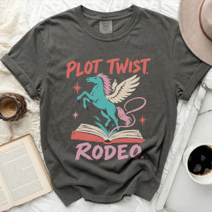 Grey t-shirt with "Plot Twist Rodeo" text and a winged unicorn on an open book.
