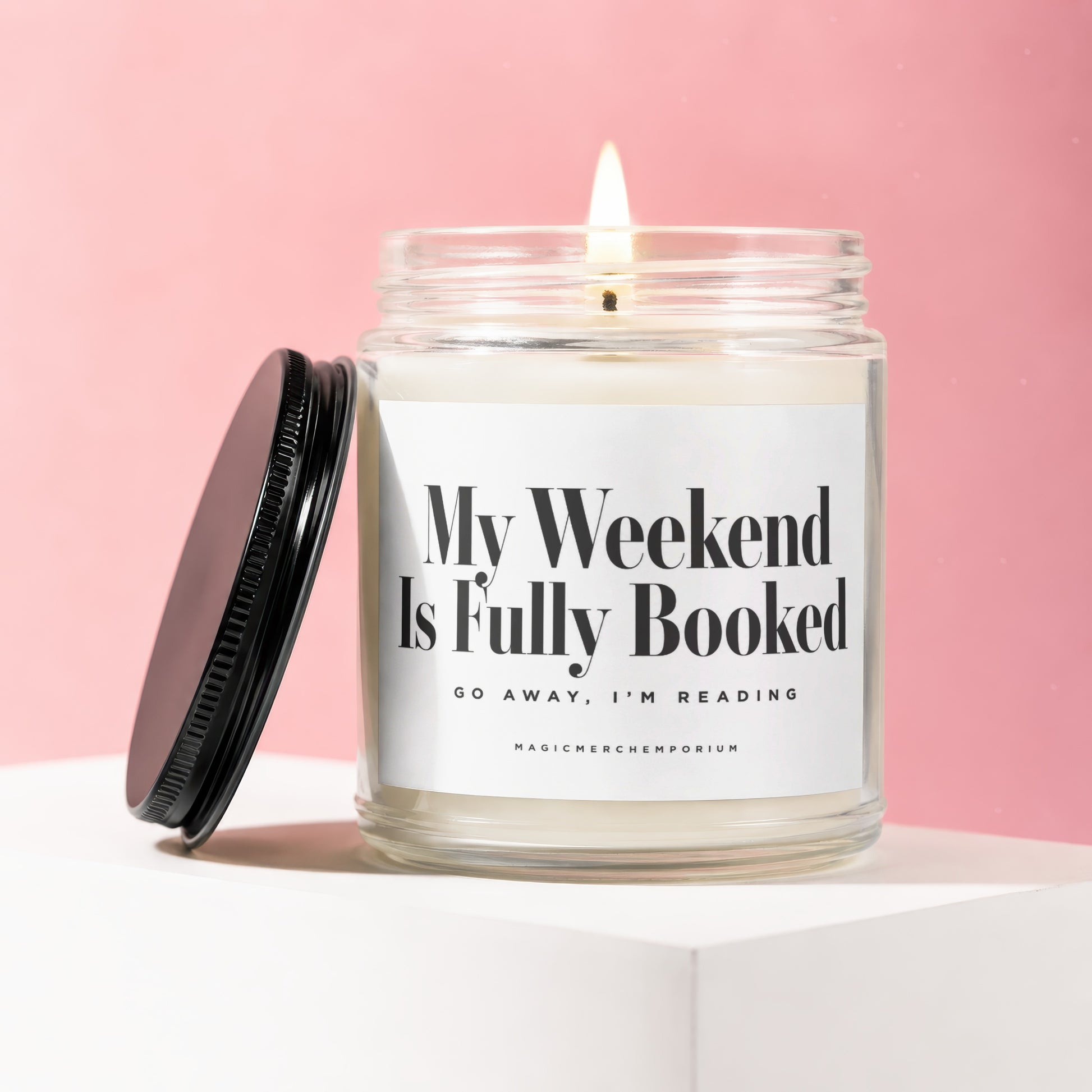 Lit candle with text "My Weekend Is Fully Booked Go Away, I'm Reading" on a pink background.