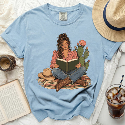 Blue t-shirt with a graphic of a woman reading by a cactus.