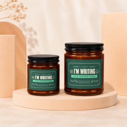 Two amber glass candles with green labels reading "I'M WRITING IT'S GOING FINE".