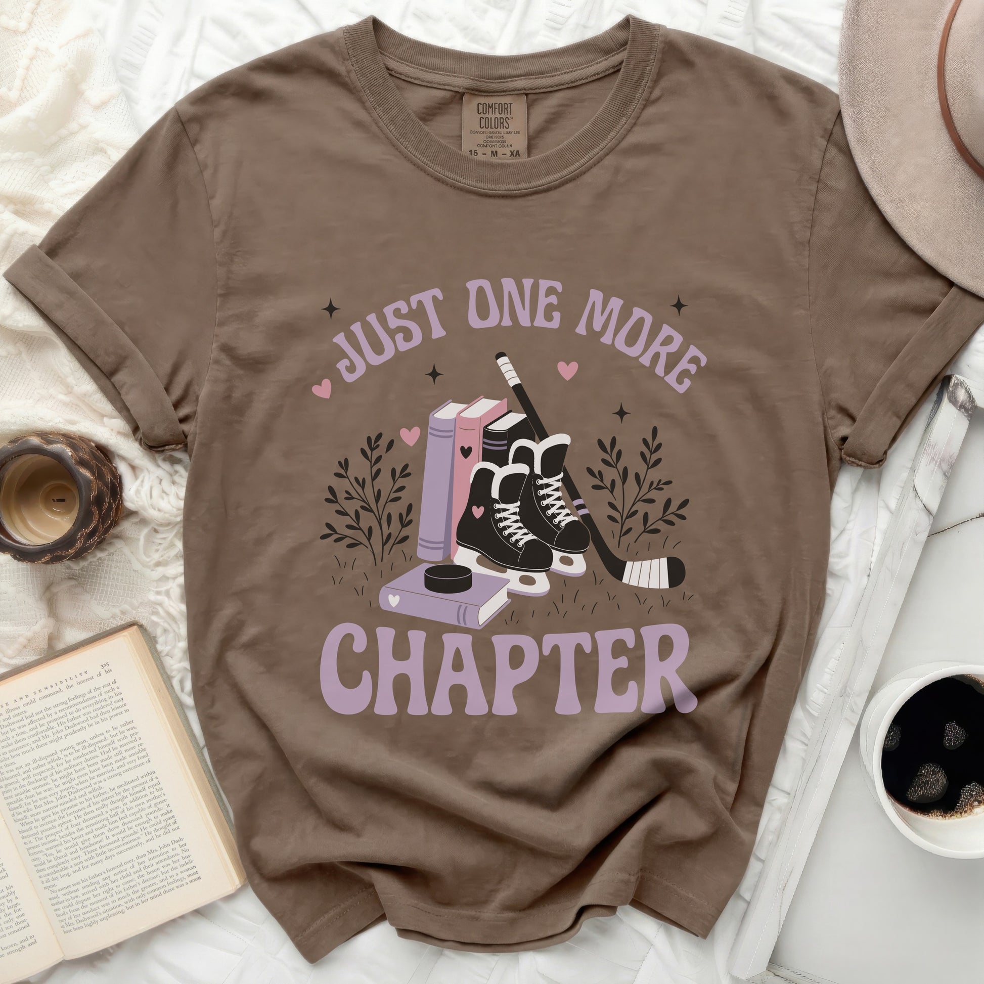 Brown t-shirt with "Just One More Chapter" and books, skates, and hockey stick design.