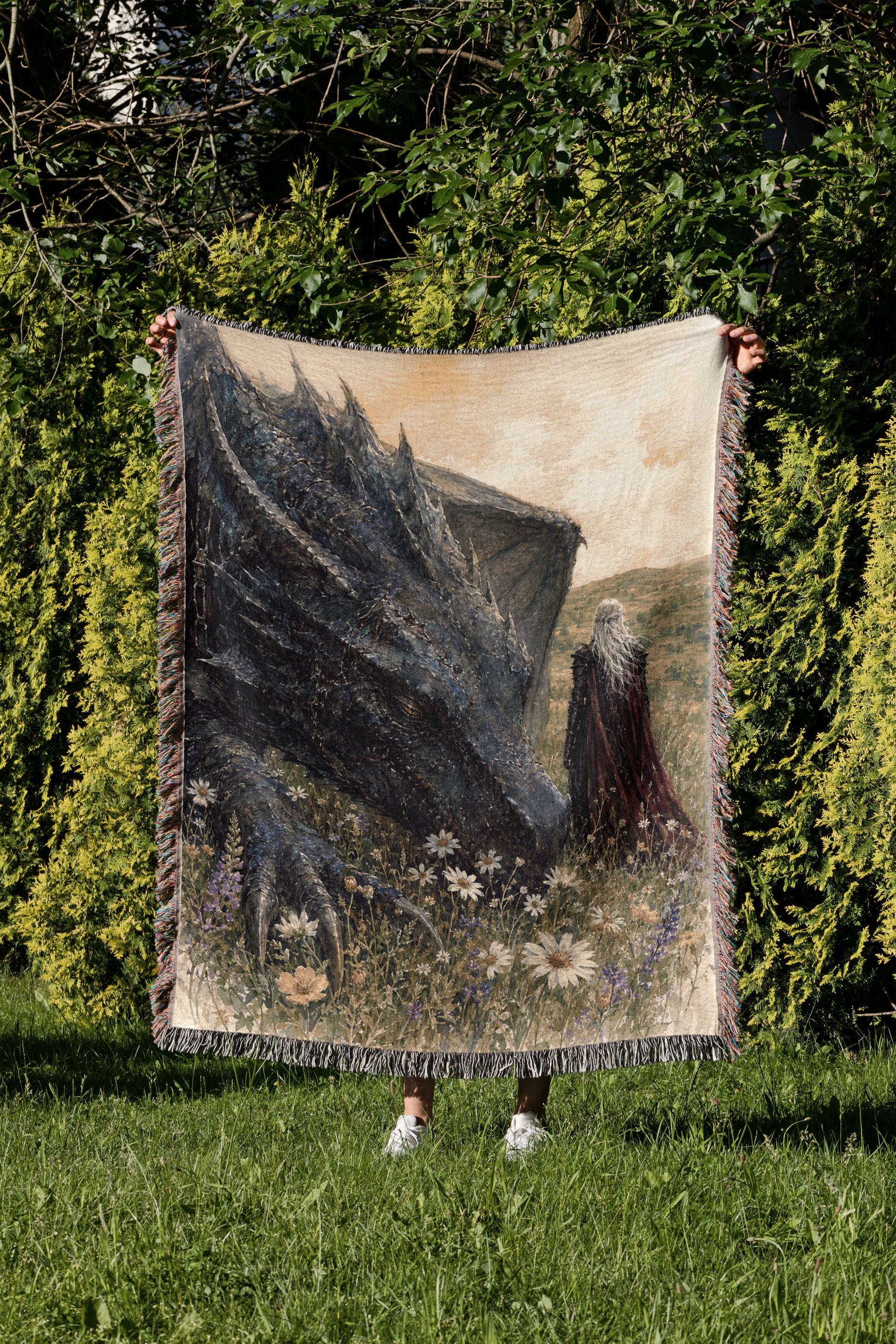 A person is holding up a large tapestry depicting a dragon in a grassy field with flowers.