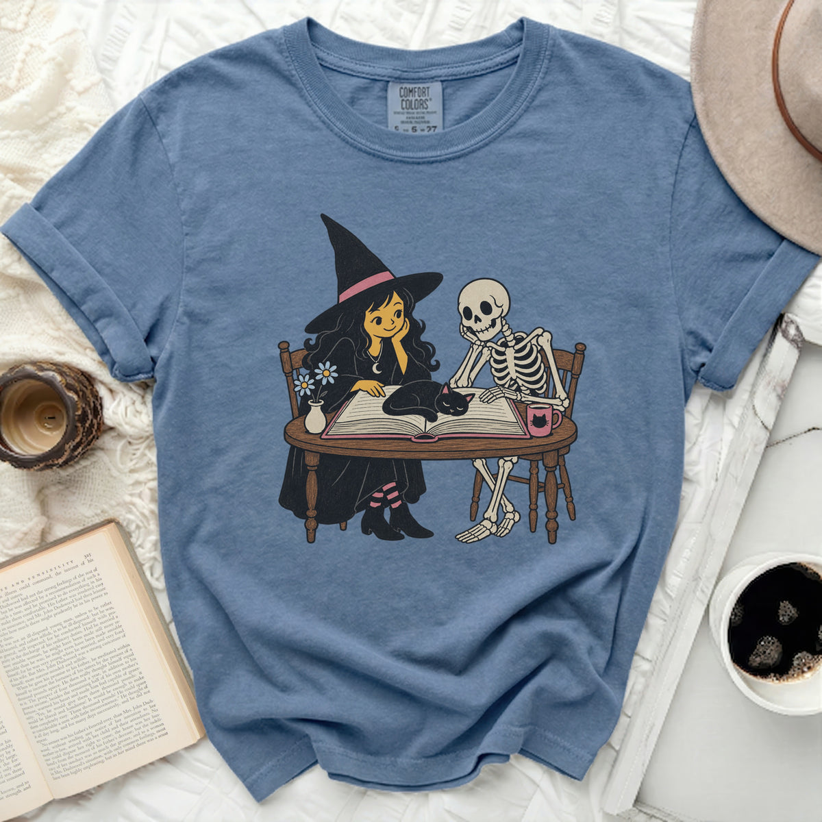 Witch, skeleton, and cat reading a book on a blue t-shirt.