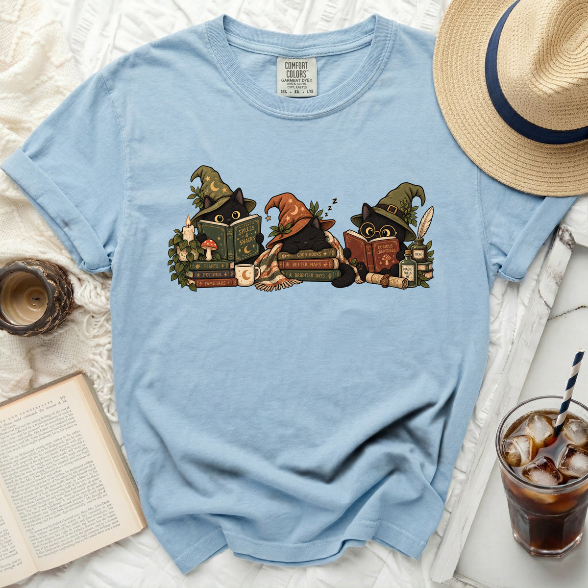 Light blue t-shirt with print of three black cats in witch hats reading books.