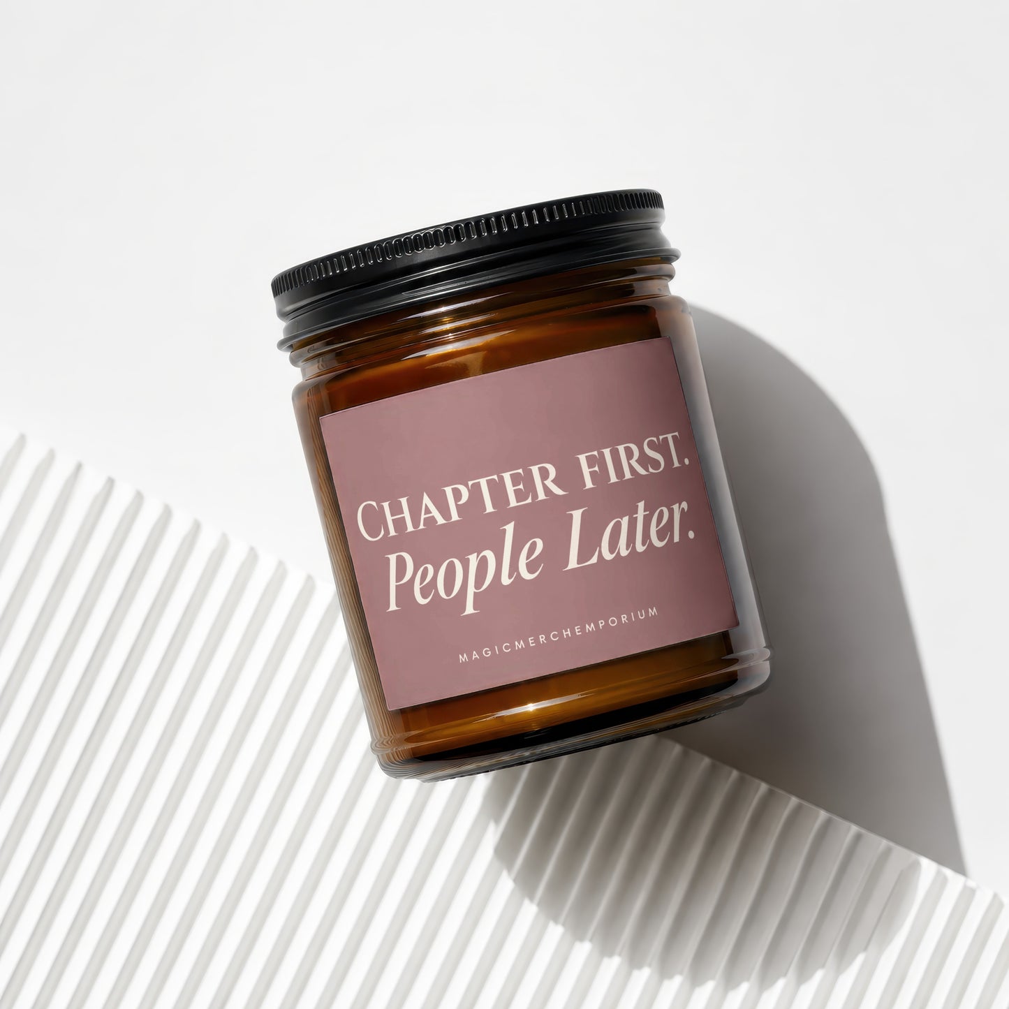 Amber glass candle with black lid and pink label reading "Chapter First. People Later."