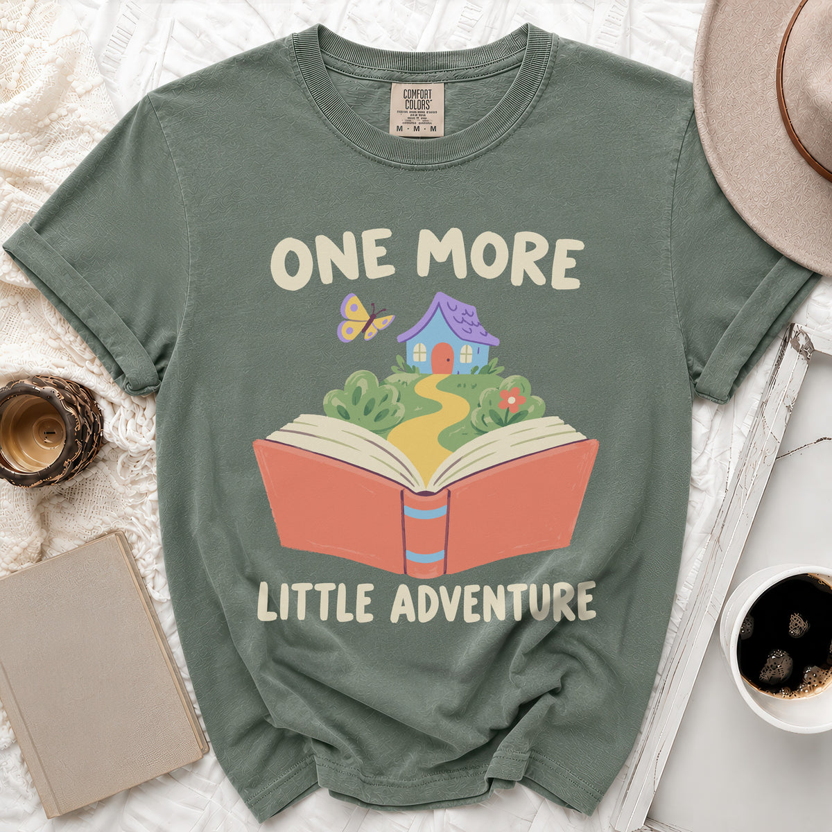Green t-shirt with "ONE MORE LITTLE ADVENTURE" text and book graphic.