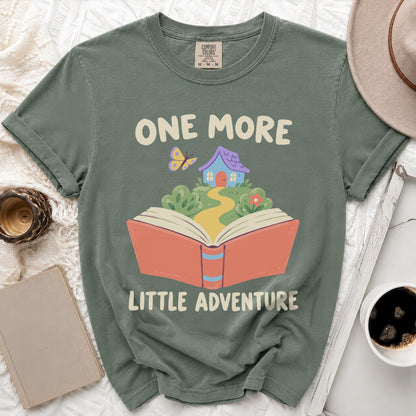 Green t-shirt with "ONE MORE LITTLE ADVENTURE" text and book graphic.