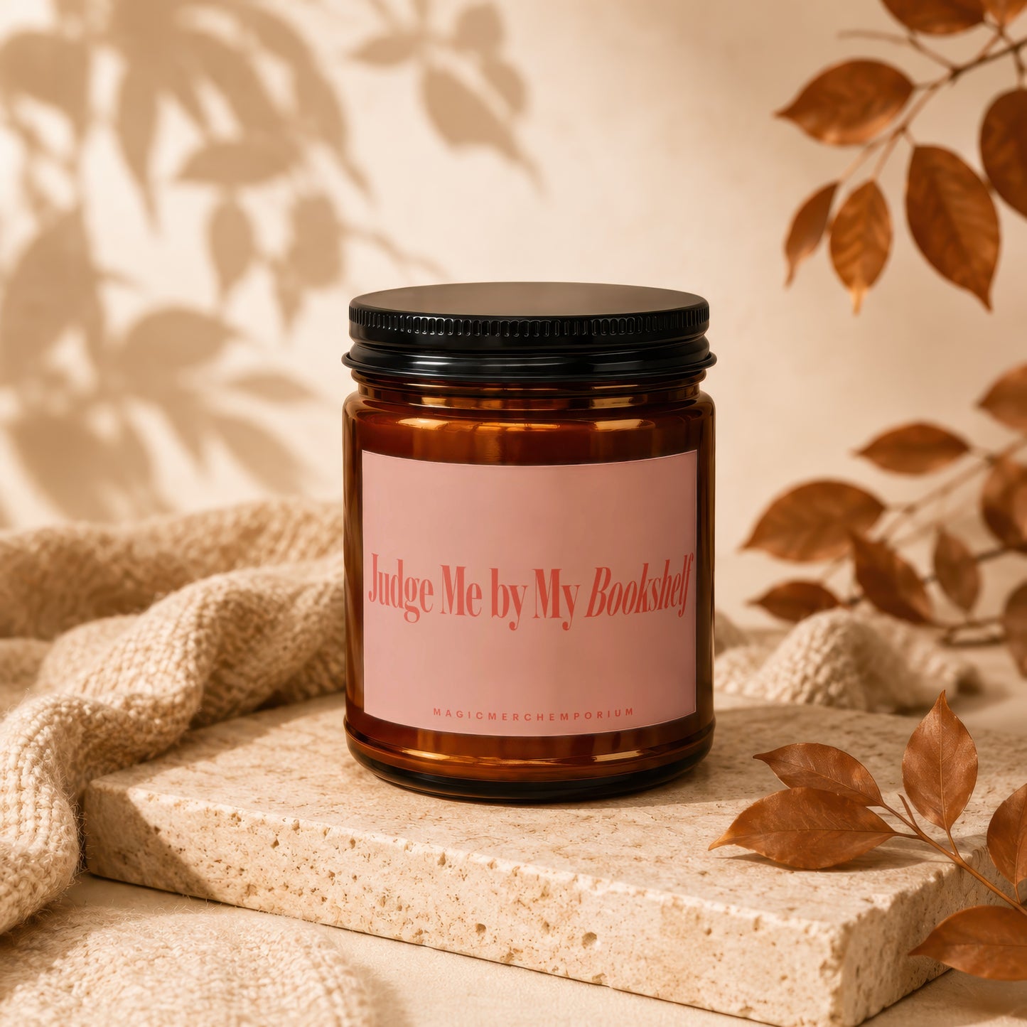 Amber jar candle with pink label reading "Judge Me by My Bookshelf."