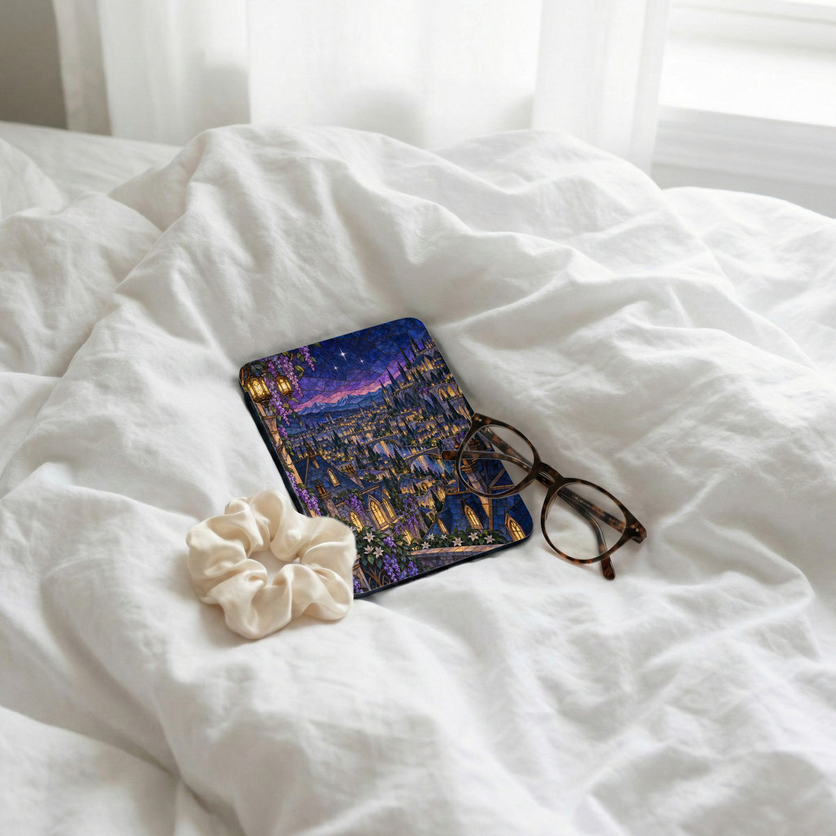 Book with stained glass castle design, scrunchie, and glasses on white bedding.