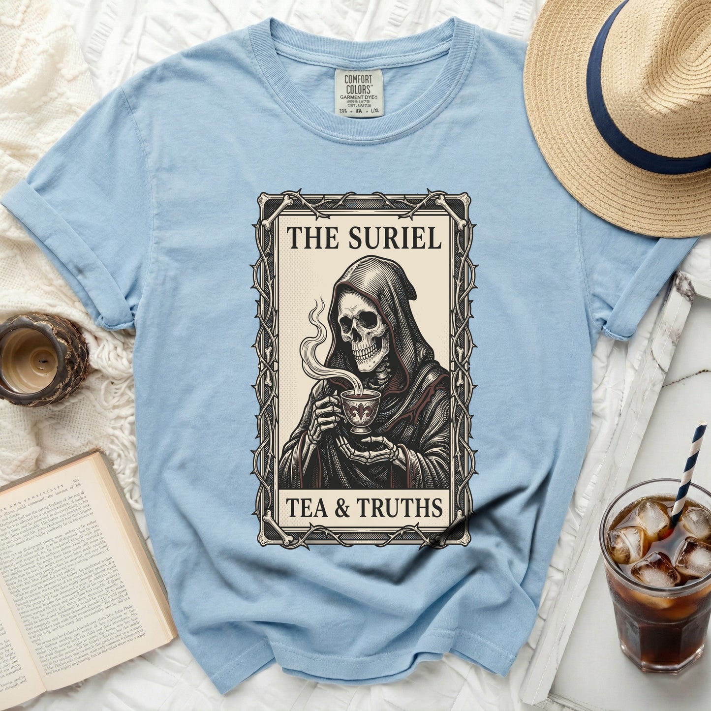 Light blue t-shirt with a grim reaper holding a teacup graphic and text "THE SURIEL TEA & TRUTHS".
