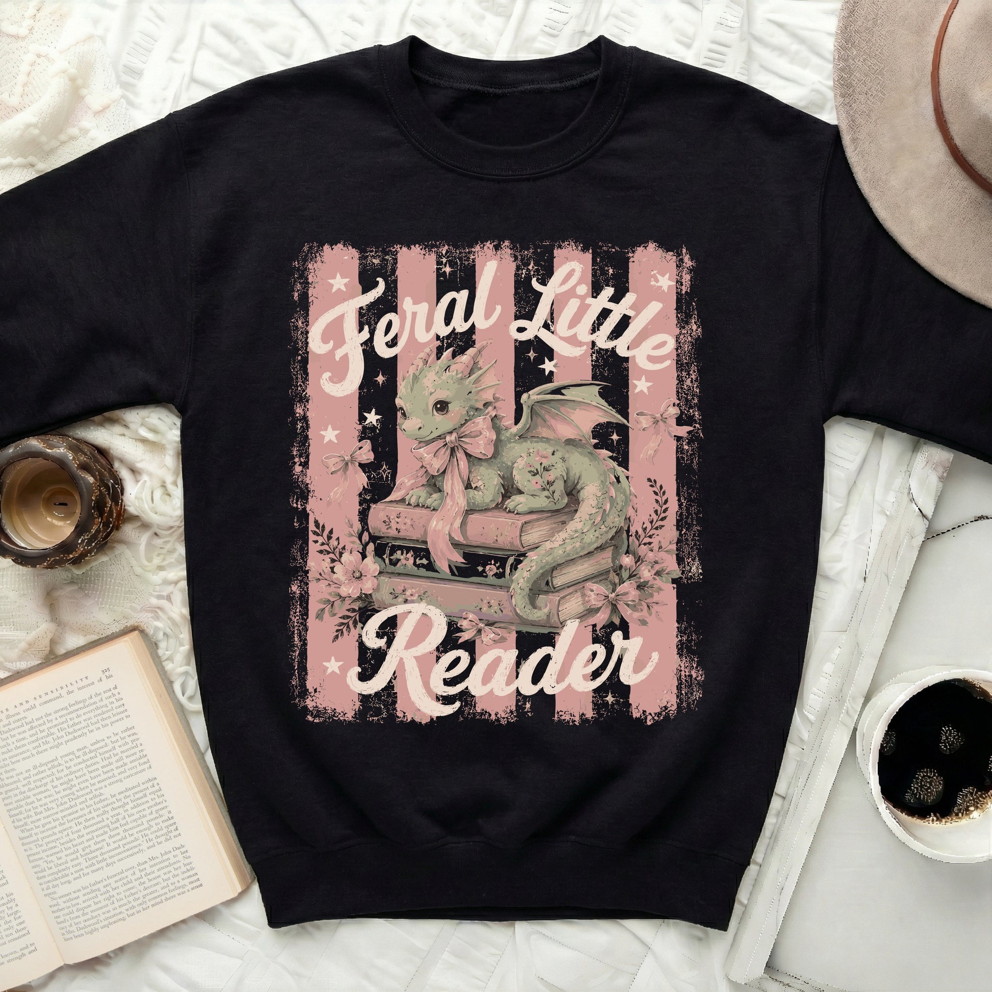 Black sweatshirt with a green dragon reading on books, text "Feral Little Reader".