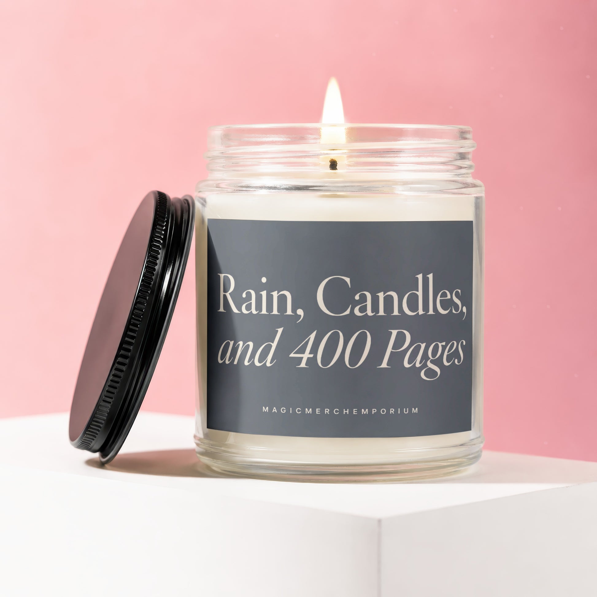 Glass jar candle with lit wick, black lid, and label reading "Rain, Candles, and 400 Pages".