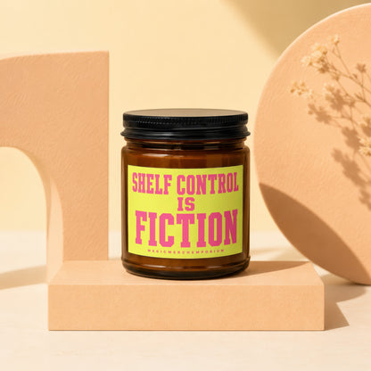 Amber jar candle with black lid, "Shelf Control is Fiction" in pink text on yellow label.