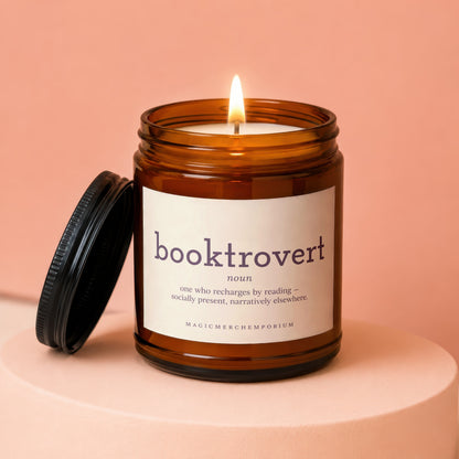 Amber jar candle with lit flame, features "booktrovert noun" definition label.