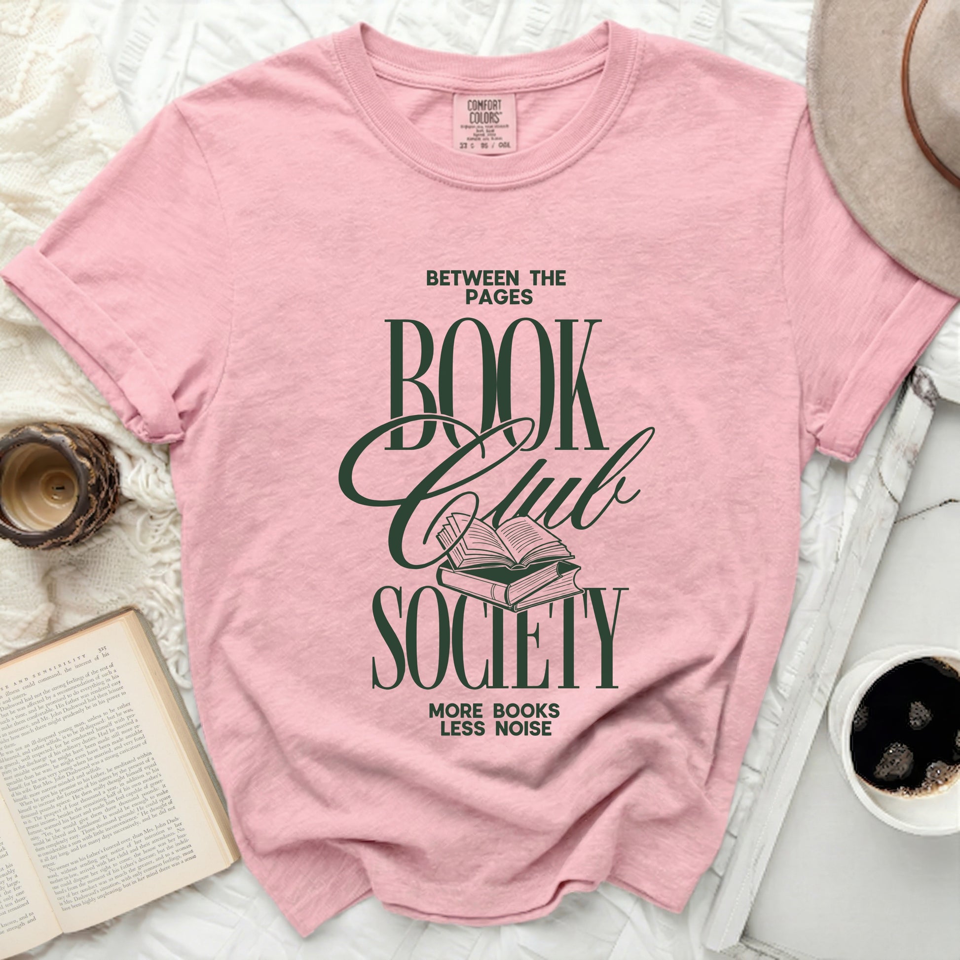 Pink t-shirt with green text "Between the Pages Book Club Society" and an open book.