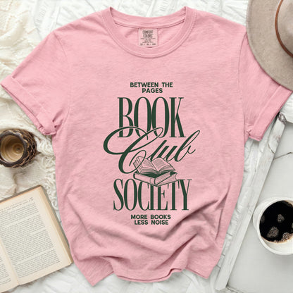 Pink t-shirt with green text "Between the Pages Book Club Society" and an open book.