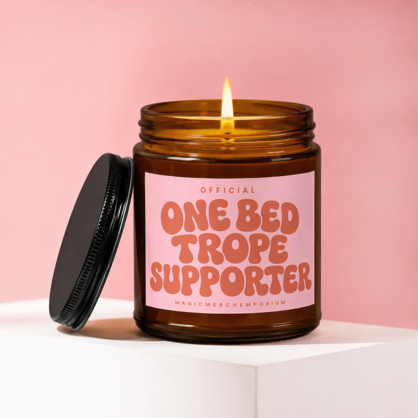 Amber jar candle with a lit wick, pink label reading "OFFICIAL ONE BED TROPE SUPPORTER".