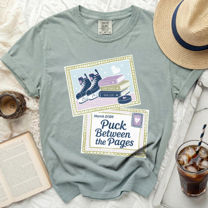 Dusty blue t-shirt with "Puck Between the Pages" and books graphic.
