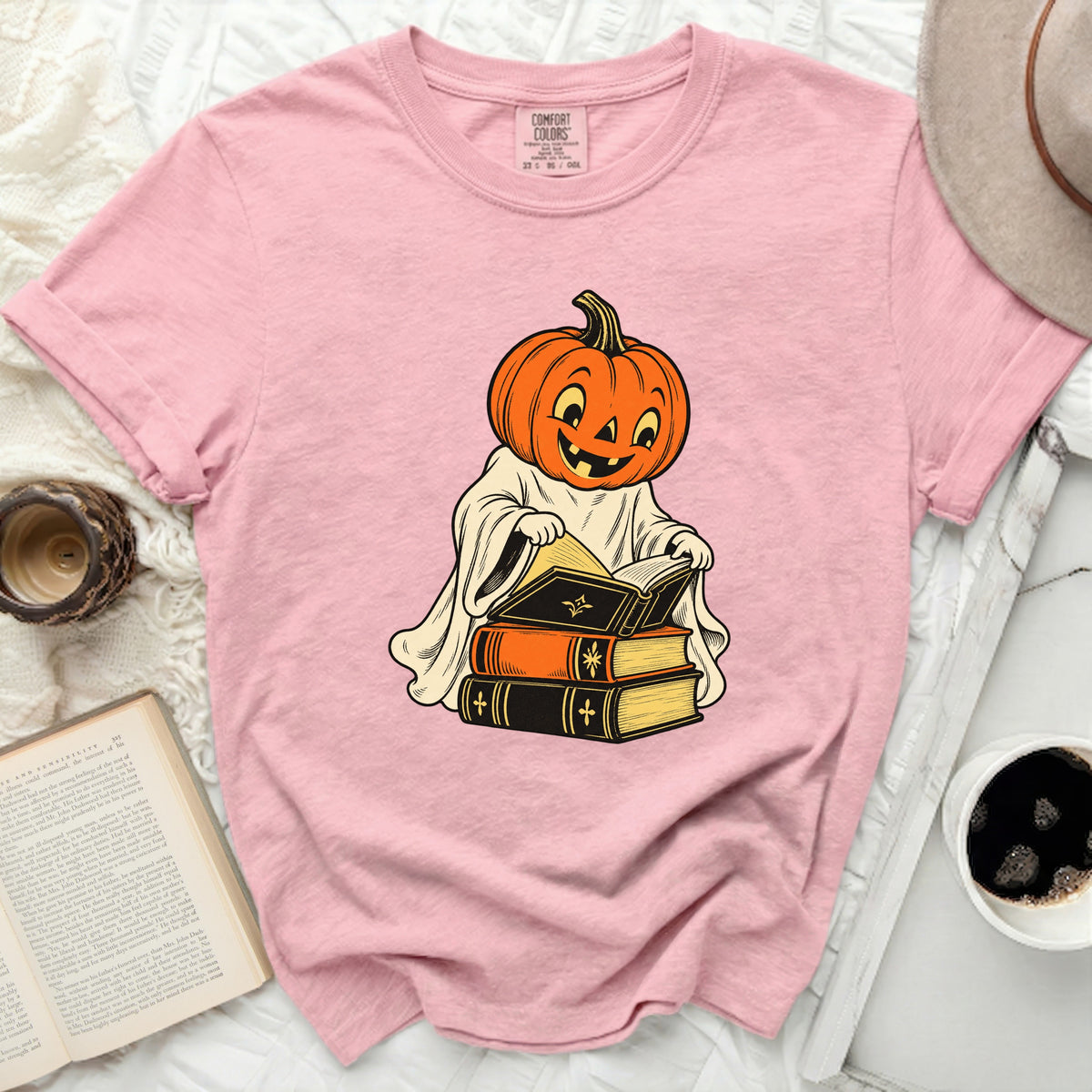 Pink t-shirt with a ghost-like figure wearing a pumpkin head reading books.