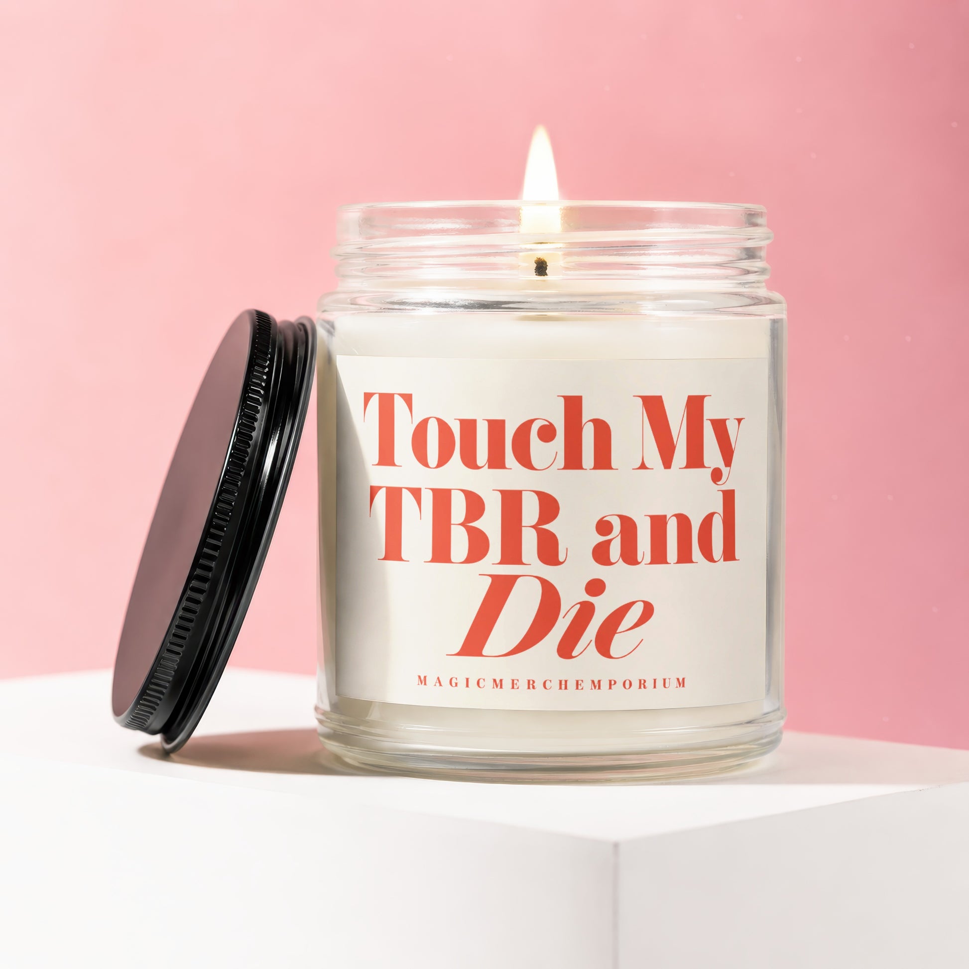 Glass candle with lit wick, black lid, and label reading "Touch My TBR and Die".