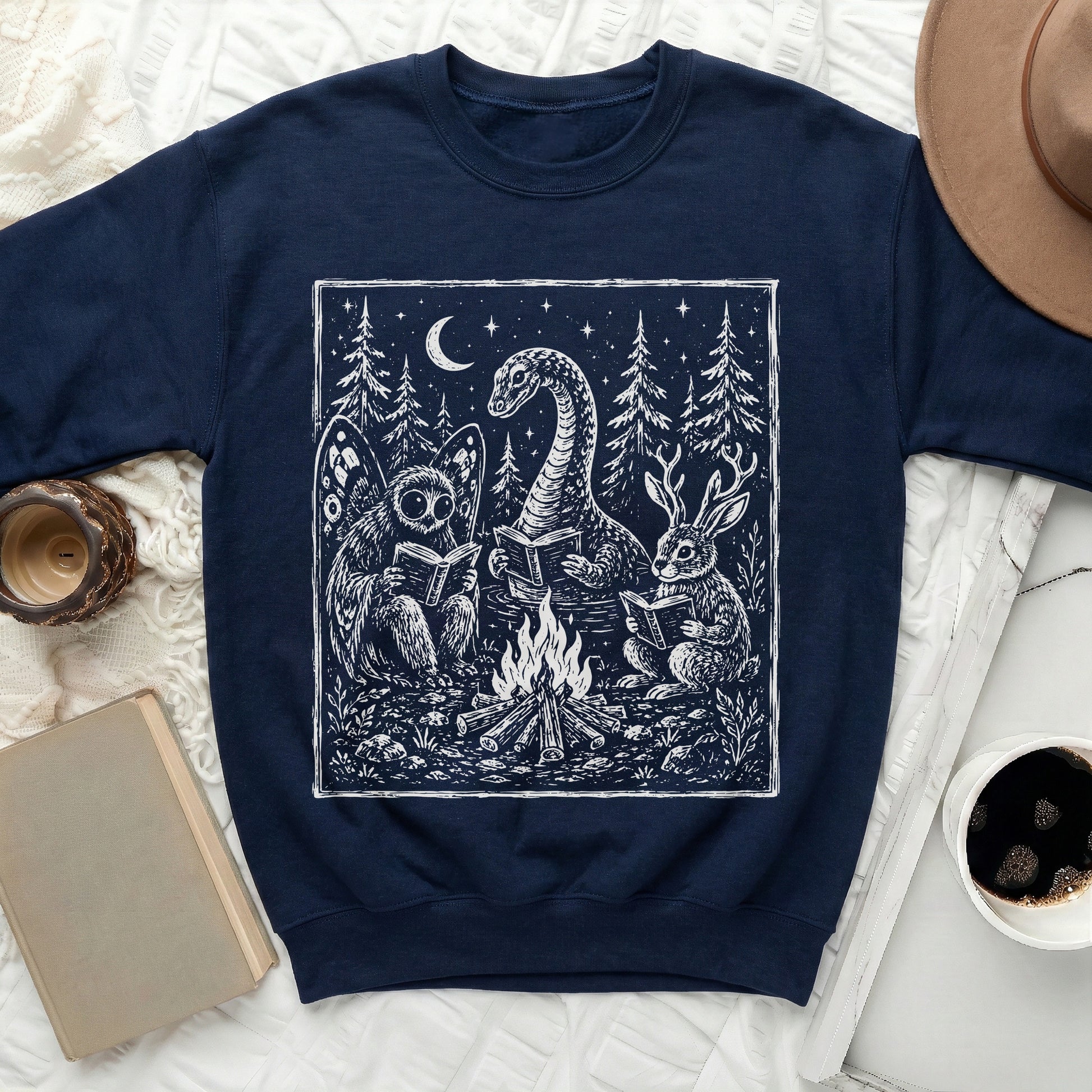 Navy sweatshirt with white graphic of mythical creatures reading by a campfire.